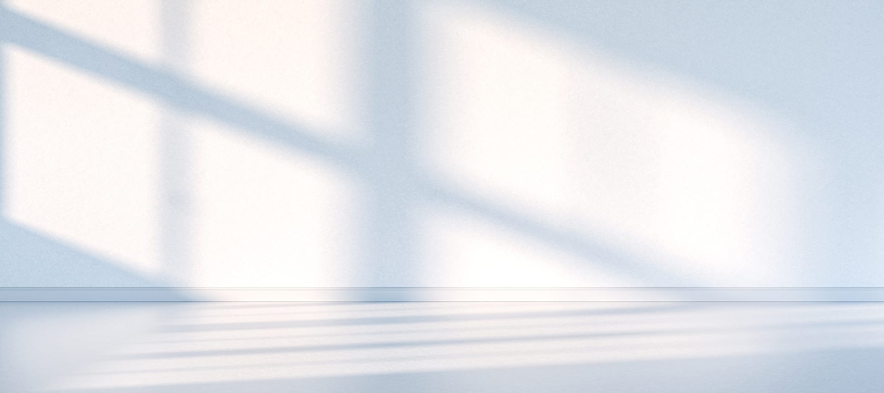 A wall with natural sunlight peaking in through a window, showing the shadows of the window.