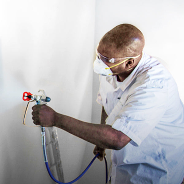 A man using a Graco paint sprayer on a wall. Graco Spray Equipment is available at Harris Paints in the Caribbean.