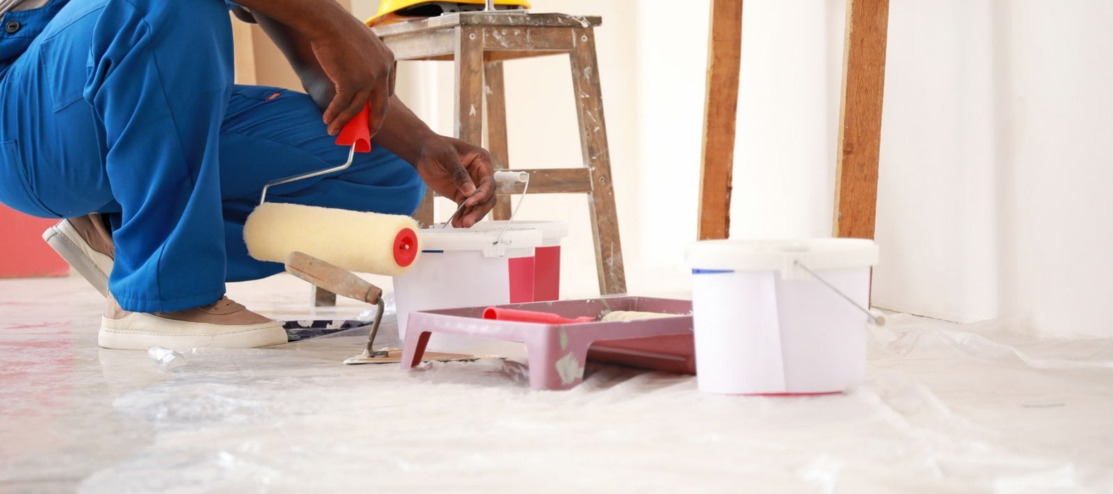 painting professional kneeling down to pour paint into a paint tray on a job site