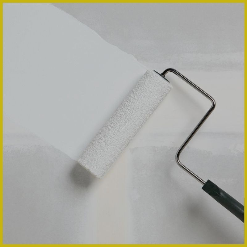 paint roller frame and roller against fresh drywall rolling on a fresh coat of primer